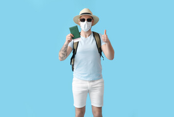 Male tourist in medical mask showing thumb-up on color background