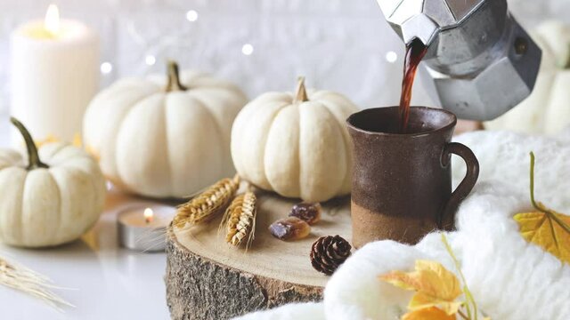 Autumn mood. Pouring black coffee in a cup with white decorative pumpkins, knited plaid and burning candles. Happy Thanksgiving  or Hello Autumn concept