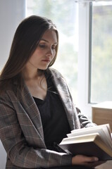 a girl with long hair is reading a book by the window