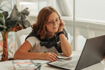 A teenage girl with glasses looks at a laptop