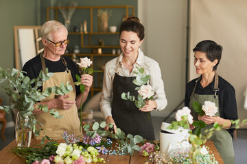 Waist up portrait of three creative florists arraigning flower compositions in workshop