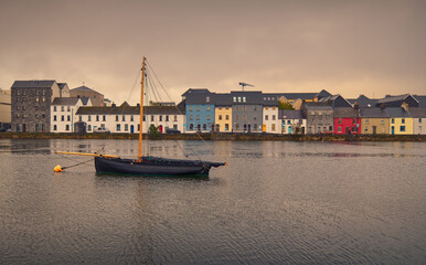 Fototapeta premium Beautiful cityscape scenery with old wooden fishing boat named Galway hooker in the Corrib River with colorful houses in the background at Claddagh in Galway city, Ireland 