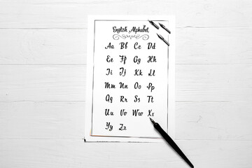 Paper with alphabet and nib pen on white wooden background