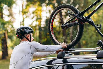 Man cyclist wearing in cycling clothes and protective helmet instals his mountain bike on the car...
