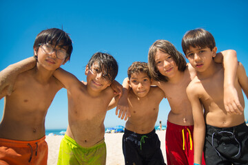 Portrait of preteen boys embracing and smiling at camera on beach. Multiethnic friends spending vacation at seaside. Summer vacation and friendship concept