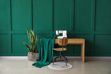 Tailor's workplace with sewing machine, cloth and houseplant near green wall