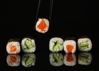 Chopsticks taking maki roll with salmon on dark background