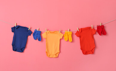 Baby clothes and socks hanging on rope against color background
