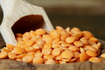 Closeup of red lentils in a bowl with a scoop. Dried red lentils in a wooden bowl on wooden background.