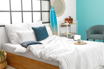 Comfortable bed with laptop, cup and earphones in stylish room