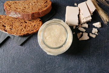 Fototapeta na wymiar Glass jar with fresh sourdough and bread slices on black background