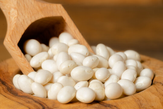 Closeup of little white dry beans in a bowl with a scoop. Dried white beans in a wooden bowl on wooden background .