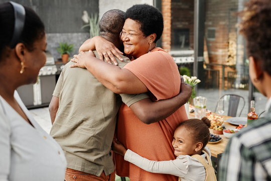 Waist up portrait of mature African-American woman embracing friend during family gathering at dinner party outdoors, copy space