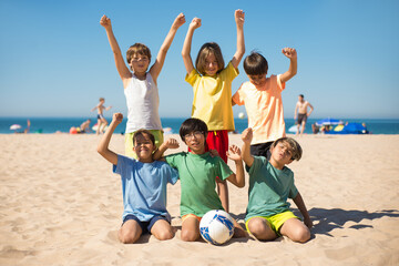 Portrait of joyful preteen boy friends on beach. Group of multiethnic kids standing and sitting on...