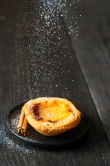 Icing Sugar  pouring on pastel de nata on wooden table. Typical Portuguese egg pastry