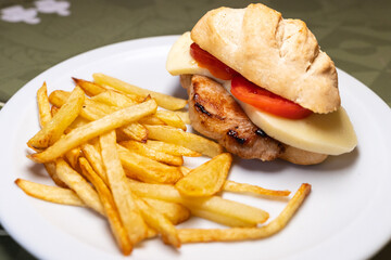 Close up view of a plate with a pork, tomato and cheese sandwich with fries