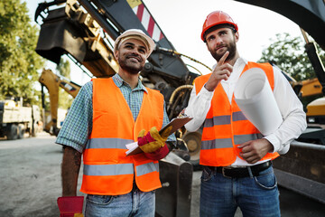 Two men engineers discussing their work standing against construction machines