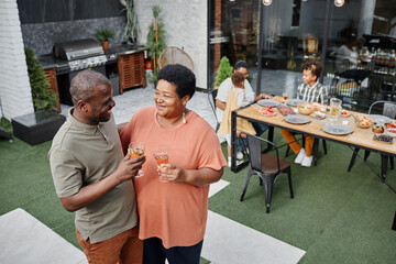 High angle portrait of mature African-American couple chatting while enjoying family gathering at outdoor terrace, copy space