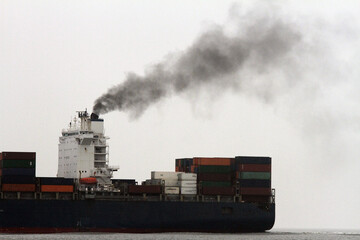 CO2 Ausstoss: ein Container Frachtschiff stößt schwarzen Rauch aus vor weißem Himmel