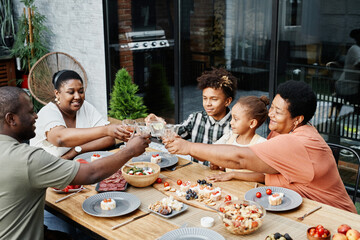 Portrait of big African-American family clinking glasses while enjoying dinner together outdoors...