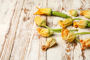 Fresh zucchini with flowers on light wooden background, closeup