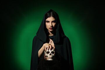 Young witch with skull on dark color background