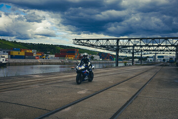 Motorradfahrer auf Schienen im Hafengebiet und Wolken im Hintergrund