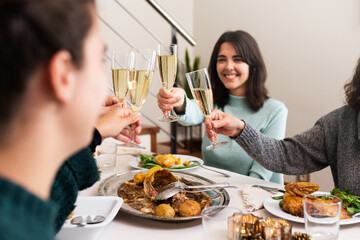 Young woman toast with champagne to celebrate Christmas with family at home. Selective focus on hand and glass.