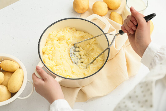 Woman preparing tasty mashed potatoes on light background, closeup