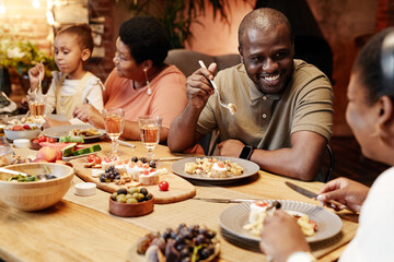 Warm toned portrait of happy African-American family enjoying dinner together outdoors with focus...