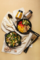 Frying pans with different vegetables and spices on color background