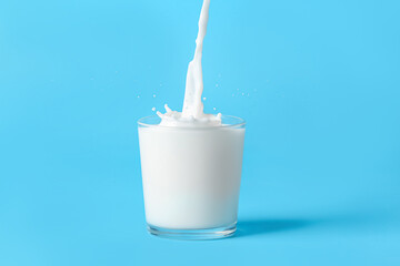 Glass of milk pouring with splash on color background