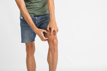 Young man scratching himself on light background