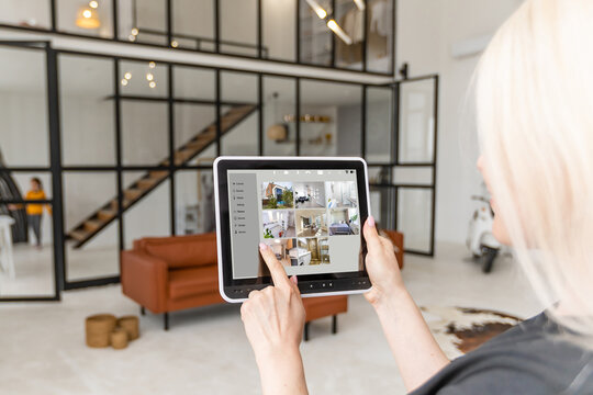 Photo of a young woman sitting by the window and using digital tablet at home.
