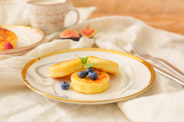 Plate with cottage cheese pancakes and blueberries on light fabric background