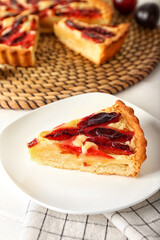 Plate with piece of tasty plum pie on light background, closeup