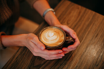 Young brunette girl sitting in coffee in a brown sweater with a mug of coffee
