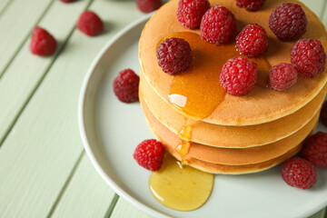 Plate of tasty pancakes with honey and berries on color wooden background