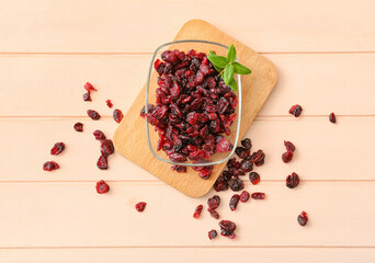 Bowl with tasty dried cranberries on color wooden background