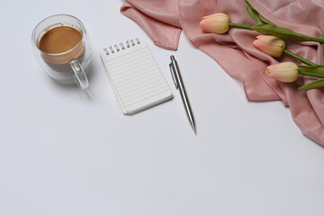 Empty notebook, coffee cup and pink tulips on white table.