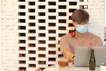Fototapeta na wymiar Asian man wearing healthy mask and working with laptop at home. Quarantine situation and work from home concept.