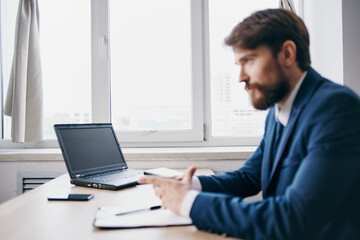 bearded man sitting at a desk in front of a laptop finance official
