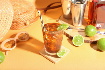 Glass of refreshing Long Island iced tea, limes and sunglasses on color background