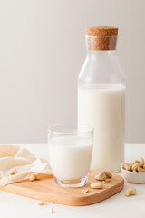 A glass and bottle of milk with nuts on white table.