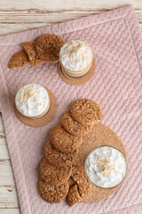 Glasses of tasty latte with nuts and cookies on white wooden background