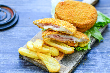 
 Crispy  deep fried home made     chicken Cordon bleu with cheese   and ham  and french fries on wooden rustic background.  