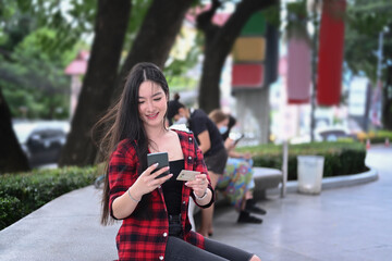 Happy young woman using mobile phone and holding credit card for payment online.