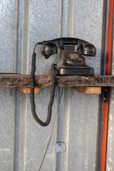 Close up of an old black analog phone on a wooden shelf in a booth made of corrugated iron.