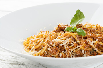 Healthy plate of Italian spaghetti topped with a tasty tomato and ground beef Bolognese sauce and fresh basil on a rustic white wooden table