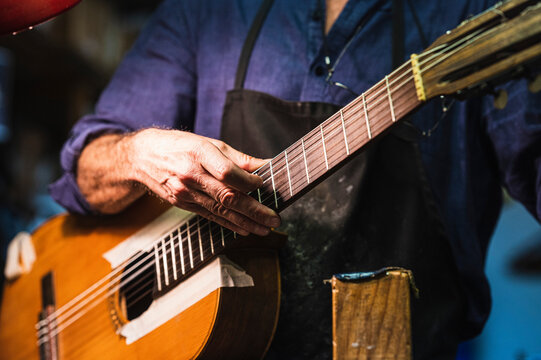 Senior luthier checking strings while playing guitar in workshop